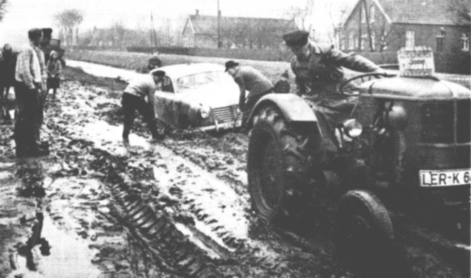 Ostrhauderfehn, 21. Januar1957: Gerd Prahm in der 2. Sdwieke ist schwer erkrankt. Doktor Graef kommt - und bleibt stecken. Mit seinem Trecker zieht Wilke Junker ihn aus dem verschlammten Weg. Bcker Friedrichs (Foto) versucht ebenfalls, mit dem Auto wegzukommen. Auch er bleibt stecken, und erneut ist die Hilfe der Nachbarn erforderlich. Von rechts: Wilke Junker, Eduard Friedrichs, Karl Bttcher, Hermann Lken und Hans Abels. Der Kranke Gerd Prahm wurde spter auf einer Trage bis zum Middendorfweg gebracht, wo der Krankenwagen vorsichtshalber stehen geblieben war. - Wer dieses Bild lnger betrachtet, der kann verstehen, da die Ostrhauderfehner stolz sind auf ihre heutigen Teerstraen.