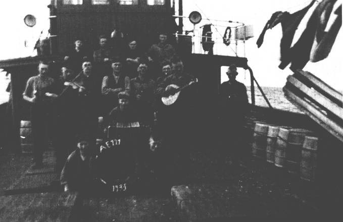 Auf diesem Motorlogger AE 121 von 1935 ging es lustig zu. Ganz rechts steht Kapitn Johannes Meiners aus Westrhauderfehn, der in Burlage wohnte. Links neben dem Rettungsring sitzt Heinrich Meiners, rechts Johannes Behrens, und der Junge mit dem Bandoneon ist Bernhard Meiners. Ganz oben stehen von links Heinrich Bning, Johannes Droste, Heinrich Osteresch und Heinrich Grssing. Die mittlere Reihe von links: Johann Fokko Bohlmann, der Maschinenassistent aus Emden mit der Geige, unbekannt, Hermann Weber aus Burlage, Bernhard Hanneken und mit der Mandoline Johannes Grssing. Ihm schaut Hermann Meyer ber die Schulter. - Diese Motorlogger waren schon so gebaut, da sie spter als Vorpostenboote dienen konnten. Rechts hngt die Netzrolle, die zum Ein- oder Ausholen der Fischnetze diente; vorn die Luken der Netzrume. Das Foto wurde bei der Ausfahrt gemacht, denn die Mnner haben noch keine Brte, und an Bord ist noch alles sauber. Kapitn Meiners hatte gern eine lustige Mannschaft an Bord, weil die Arbeit dann besser von der Hand lief. Dem Fidelknstler wurde nur leider immer schlecht bei etwas zu hohem Seegang. Solch ein ,,gemischtes Orchester" traf man selten an, aber musiziert und gesungen wurde eigentlich auf allen Schiffen.