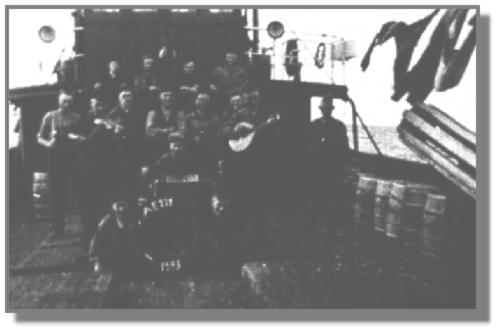 Auf diesem Motorlogger AE 121 von 1935 ging es lustig zu. Ganz rechts steht Kapitn Johannes Meiners aus Westrhauderfehn, der in Burlage wohnte. Links neben dem Rettungsring sitzt Heinrich Meiners, rechts Johannes Behrens, und der Junge mit dem Bandoneon ist Bernhard Meiners. Ganz oben stehen von links Heinrich Bning, Johannes Droste, Heinrich Osteresch und Heinrich Grssing. Die mittlere Reihe von links: Johann Fokko Bohlmann, der Maschinenassistent aus Emden mit der Geige, unbekannt, Hermann Weber aus Burlage, Bernhard Hanneken und mit der Mandoline Johannes Grssing. Ihm schaut Hermann Meyer ber die Schulter. - Diese Motorlogger waren schon so gebaut, da sie spter als Vorpostenboote dienen konnten. Rechts hngt die Netzrolle, die zum Ein- oder Ausholen der Fischnetze diente; vorn die Luken der Netzrume. Das Foto wurde bei der Ausfahrt gemacht, denn die Mnner haben noch keine Brte, und an Bord ist noch alles sauber. Kapitn Meiners hatte gern eine lustige Mannschaft an Bord, weil die Arbeit dann besser von der Hand lief. Dem Fidelknstler wurde nur leider immer schlecht bei etwas zu hohem Seegang. Solch ein ,,gemischtes Orchester" traf man selten an, aber musiziert und gesungen wurde eigentlich auf allen Schiffen.