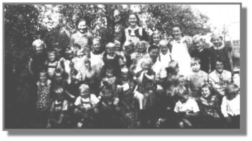 Den Westrhauderfehner Kindergarten leitete Tante Agnes, die nicht von hier war. Ihr zur Seite standen Meta Leefoge und Dita Oltmanns, die auf unserer Aufnahme aus dem Jahre 1939 im Hintergrund zu sehen sind. Annegret Stockmar, die in der oberen Reihe ganz rechts steht, konnte uns noch etliche Namen nennen. Links neben ihr steht Alfred Ohling, dann Herta und Uwe Schmidt. ber Tante Agnes steht Frieda Kretzmer, aber das Mdchen neben ihr ist unbekannt. Dann folgen die Zwillinge Karl-Heinz und Gerald Gewald. Zwischen ihnen steht dahinter Mathilde Ulpts. Das groe Mdchen mit der weien Schrze ist Martha Thomsen, und die schne Schleife ist auf dem Kopf von Anneliese Kramer befestigt. Dahinter stehen erneut Zwillinge, nmlich Rudolfine und Johanne Rosenboom. Neben ihnen ist Helmut Detmers zu erkennen, und das Mdchen ganz links wollte sich nicht zu erkennen geben. Darunter in der zweiten Reihe hockt wieder ein unbekanntes Mdchen. Dann folgen Anton Hesenius, Hildegard Detmers, die zur Seite schaut, und Karin Bernhards sowie Hilde Kramer. Die nchsten drei Kinder wollten ihren Namen nicht nennen. Die vorletzte knnte eine Bodamer sein, und das Mdchen ganz rechts ist Elfriede Jelden. Unter ihr sitzt unten ganz rechts Theo Rosenboom. Die nchsten drei Kinder sind wieder unerkannt. In der Mitte mit der schnen weien Schleife sitzt Erna Hesenius, daneben unbekannt, dann Heinz Kretzmer und ein Noormann? -